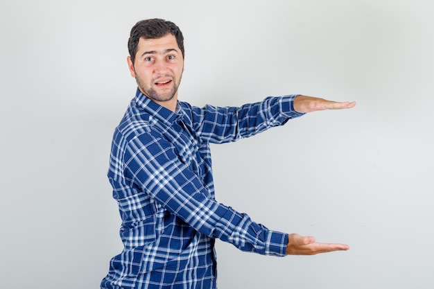 Foto gratuita joven mostrando signo de gran tamaño en camisa a cuadros