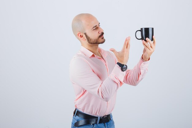 Joven mostrando taza negra en camisa rosa, vista frontal de jeans.