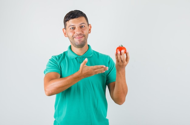 Joven mostrando tomate en la mano en camiseta verdosa y mirando feliz.