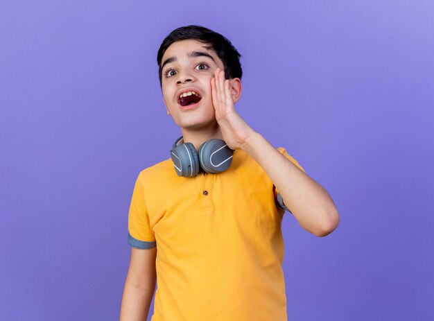 Joven muchacho caucásico con auriculares en el cuello aislado sobre fondo púrpura