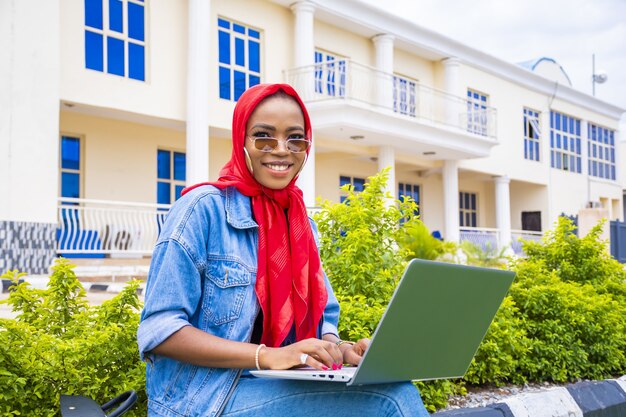 Joven mujer africana sonriendo mientras trabaja con su computadora portátil en un parque