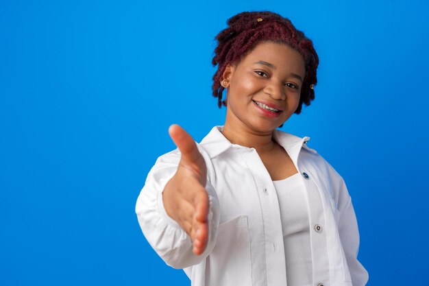 Joven mujer afro extiende la mano para apretón de manos contra el fondo azul.