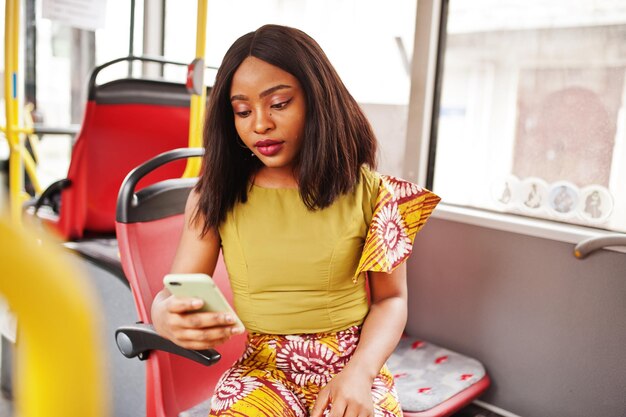 Joven mujer afroamericana con estilo montando en un autobús con teléfono móvil