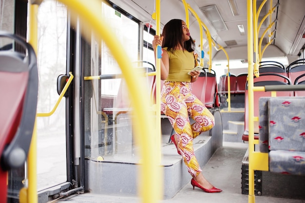 Joven mujer afroamericana con estilo montando en un autobús con teléfono móvil