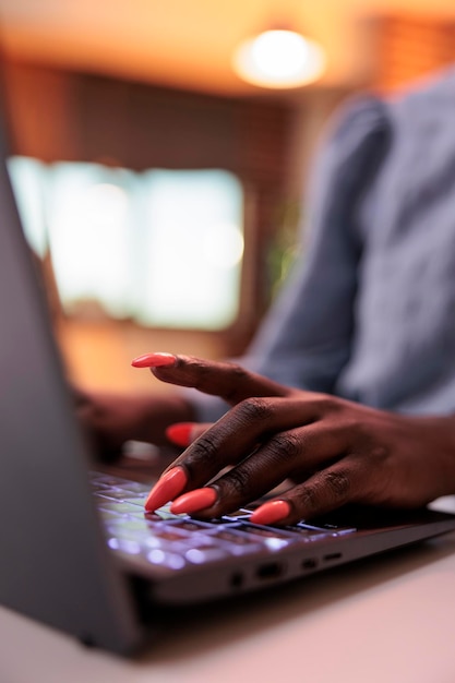 Joven mujer afroamericana independiente escribiendo en el teclado de la computadora portátil, vista de cerca en las manos. Empresaria navegando por Internet, escribiendo correos electrónicos en la computadora, enfocándose en las uñas cuidadas