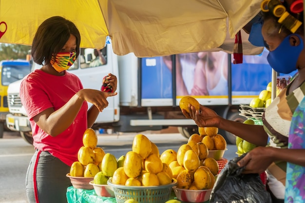 Joven mujer afroamericana con una mascarilla protectora mientras compra en un mercado de frutas