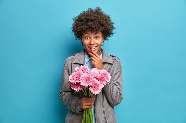 Joven mujer afroamericana de moda recibe ramo de flores de gerbera rosa de amoroso boyfiend durante la fecha