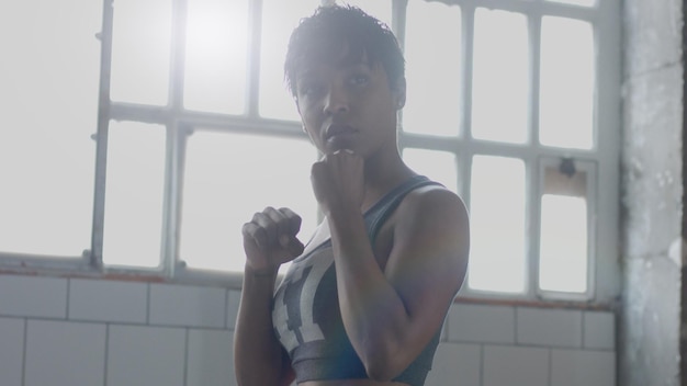 Foto gratuita joven mujer afroamericana de raza mixta hace un entrenamiento de boxeo en un loft soleado luz de contorno mirando a través de la cámara