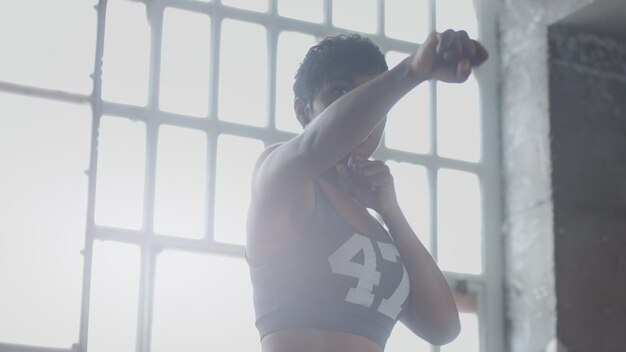 Joven mujer afroamericana de raza mixta hace un entrenamiento de boxeo en un loft soleado Luz de contorno mirando a través de la cámara