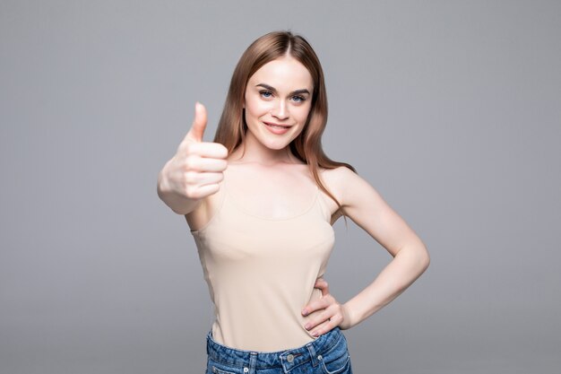 Joven mujer alegre feliz mostrando el pulgar hacia arriba aislado en la pared gris