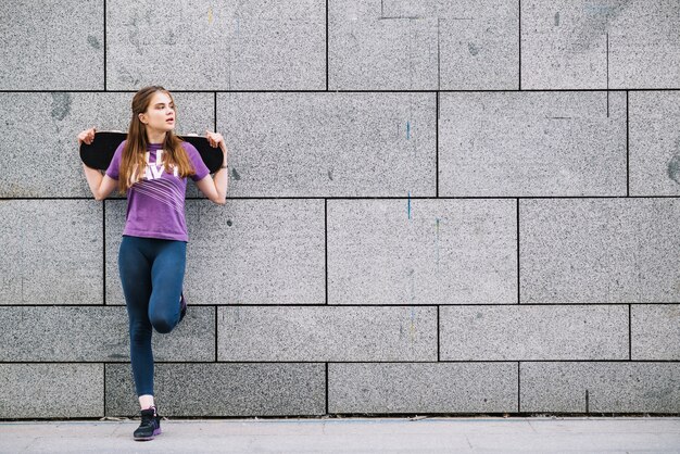 Joven mujer apoyada en una pared urbana de azulejos grises de pie sobre una pierna