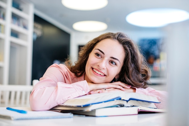 Joven mujer apoyándose en libros en la mesa