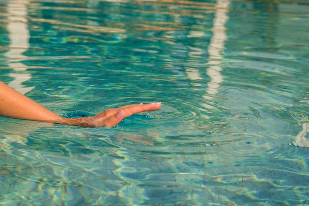 Joven mujer arrodillada en el borde de una piscina, tocando el agua tranquila con su mano.