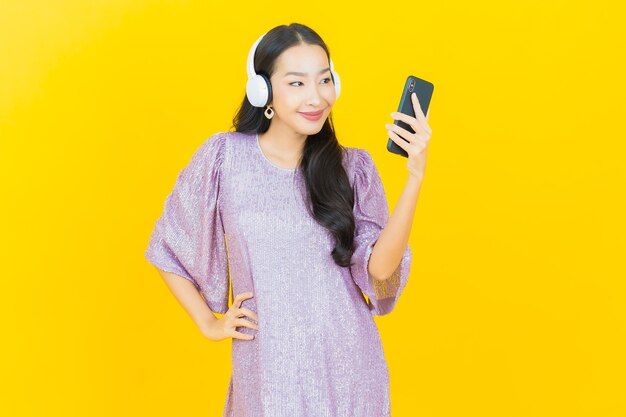 Joven mujer asiática con auriculares y teléfonos inteligentes para escuchar música en amarillo