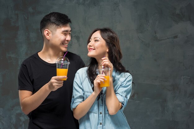 Una joven mujer asiática bonita con un vaso de jugo de naranja en las manos en el fondo gris del estudio.