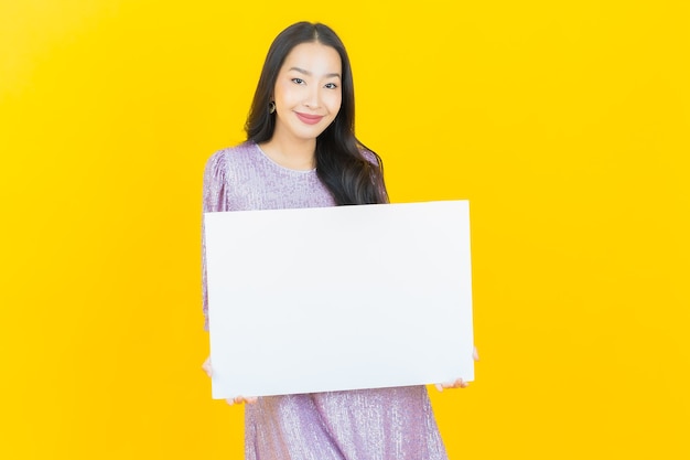 Joven mujer asiática con cartelera blanca vacía sobre amarillo