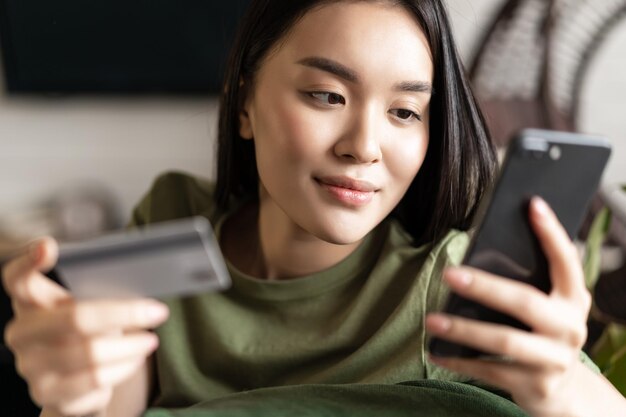 Joven mujer asiática comprando en la tienda online mediante teléfono móvil y compras con tarjeta de crédito desde casa