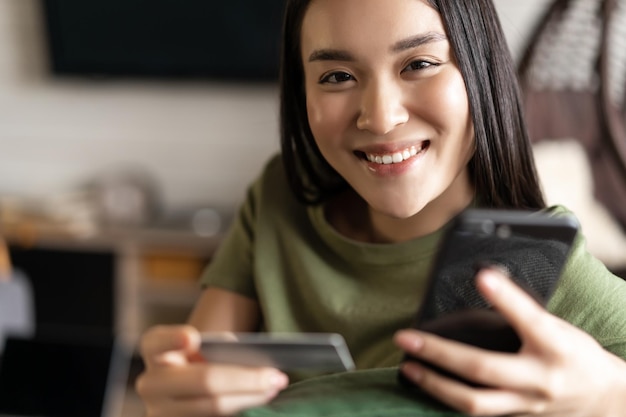 Joven mujer asiática comprando en la tienda online mediante teléfono móvil y compras con tarjeta de crédito desde casa