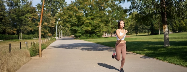 Foto gratuita joven mujer asiática fitness corriendo en el parque trotando al aire libre sonriendo complacida