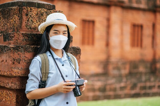 Joven mujer asiática mochilero con sombrero y máscara de protección mientras viaja en un sitio histórico