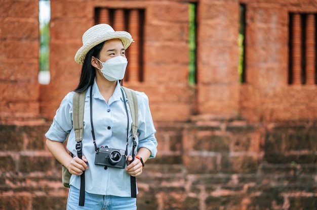 Foto gratuita joven mujer asiática mochilero con sombrero y máscara de protección mientras viaja en un sitio histórico