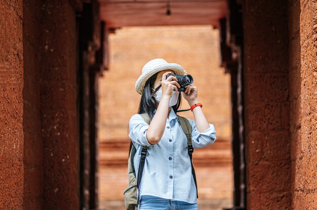 Joven mujer asiática mochilero con sombrero y máscara de protección mientras viaja en un sitio histórico