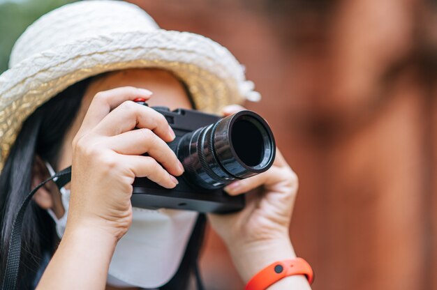 Joven mujer asiática mochilero con sombrero y máscara de protección mientras viaja en un sitio histórico