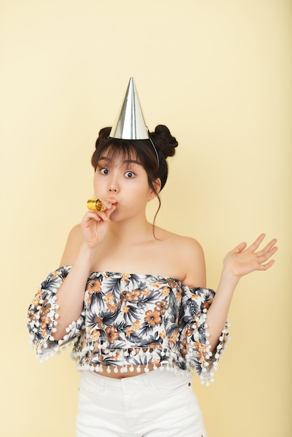 Foto gratuita joven mujer asiática posando en estudio con sombrero de fiesta y con matraca