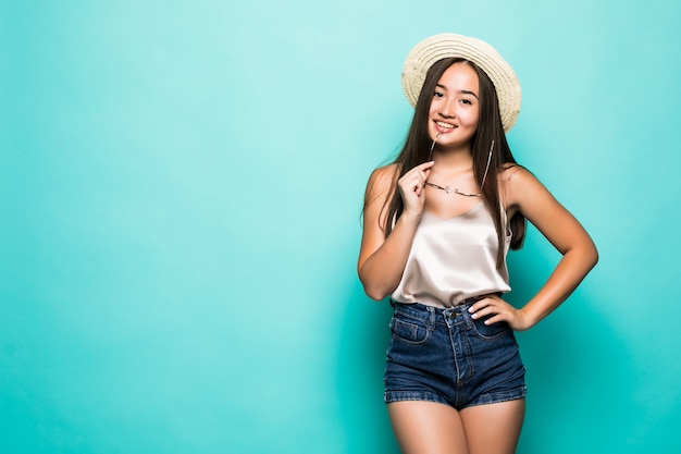 Joven mujer asiática en sombrero y gafas de sol sonriendo fondo turquesa