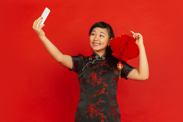 Joven mujer asiática tomando selfie con linterna china aislado en la pared roja