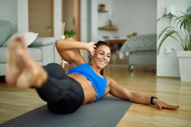 Joven mujer atlética feliz haciendo sentadillas laterales mientras hace ejercicio en la sala de estar