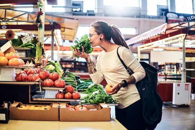 Joven mujer atractiva con tatuajes eligiendo ensalada fresca en el mercado de verduras.