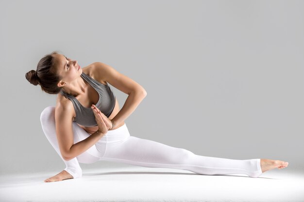 Joven mujer en Baddha Ardha Samakonasana plantean, fondo gris de estudio