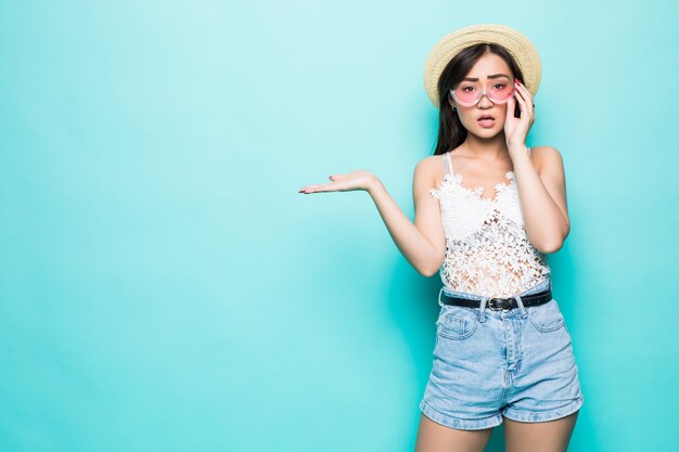 Joven mujer bastante asiática con gafas de sol gesto abierto palma aislada en la pared verde