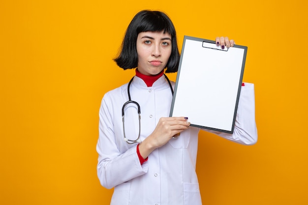 Joven mujer bastante caucásica decepcionada en uniforme médico con estetoscopio con portapapeles