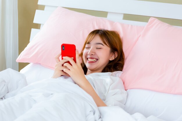 Joven mujer bonita acostada en la cama uso smartphone