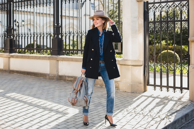 Foto gratuita joven mujer bonita con estilo sonriendo, asombrada, sorprendida, feliz, vestida con abrigo azul oscuro y jeans