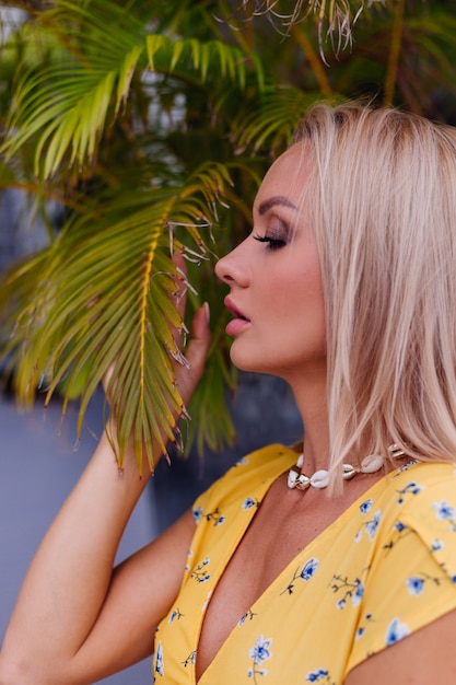 Joven mujer bonita feliz tranquila caucásica con maquillaje de noche brillante con vestido amarillo de verano y collar de conchas de mar