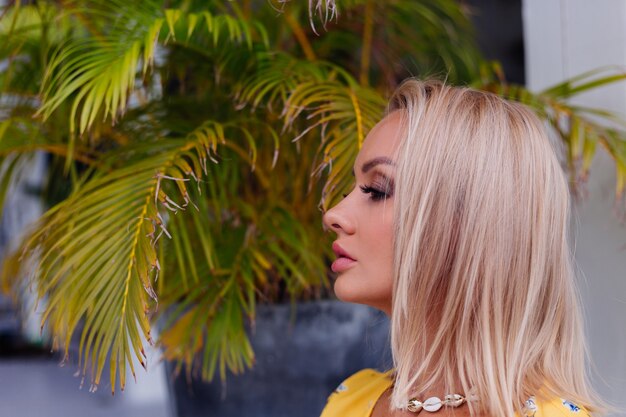 Joven mujer bonita feliz tranquila caucásica con maquillaje de noche brillante con vestido amarillo de verano y collar de conchas de mar