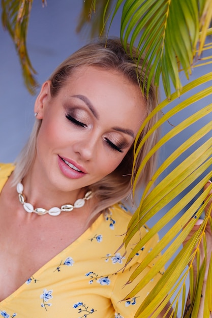 Joven mujer bonita feliz tranquila caucásica con maquillaje de noche brillante con vestido amarillo de verano y collar de conchas de mar