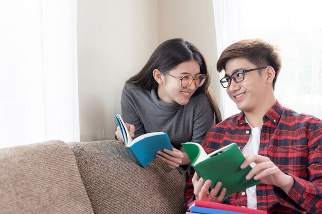 Joven mujer bonita y guapo novio con gafas y sentado para leer libros en el sofá en casa