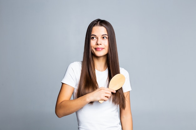 Joven mujer bonita morena peinando su hermoso cabello largo en blanco