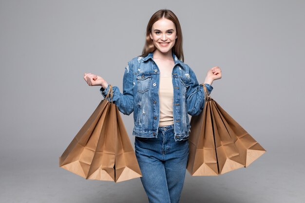 Joven mujer bonita con paquetes de compras en la pared gris