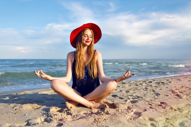 Joven mujer bonita rubia vestida con bikini negro, cuerpo delgado, disfruta de las vacaciones y divirtiéndose en la playa, largos pelos rubios, gafas de sol y sombrero de paja. Vacaciones en Bali.