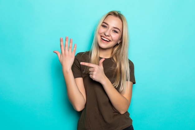 Joven mujer bonita señaló en su dedo aislado en la pared azul