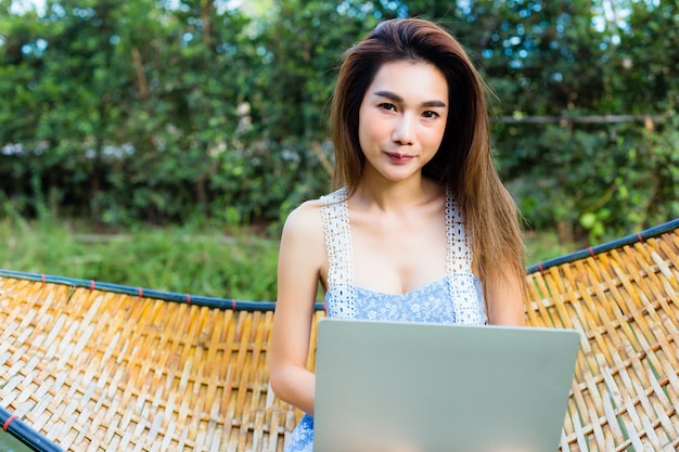 Joven mujer bonita sentada en hamaca de bambú usando laptop