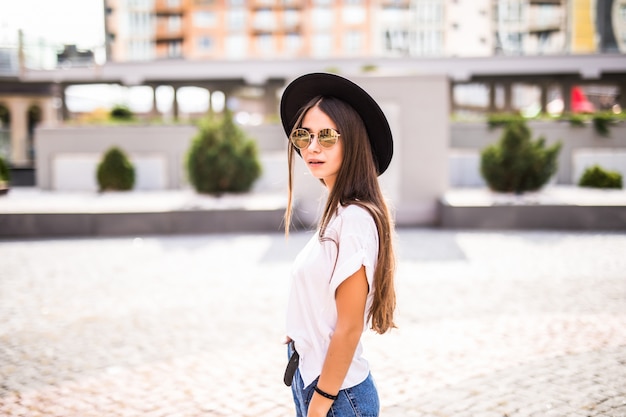 Joven mujer bonita en sombrero negro de altura completa de pie en la calle de verano