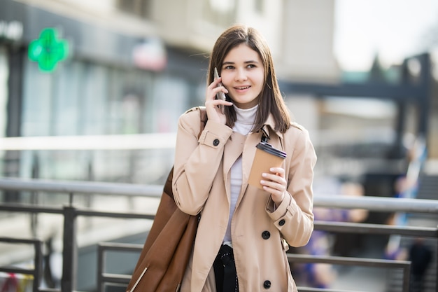 Joven mujer caminando por la calle con taza de café y teléfono