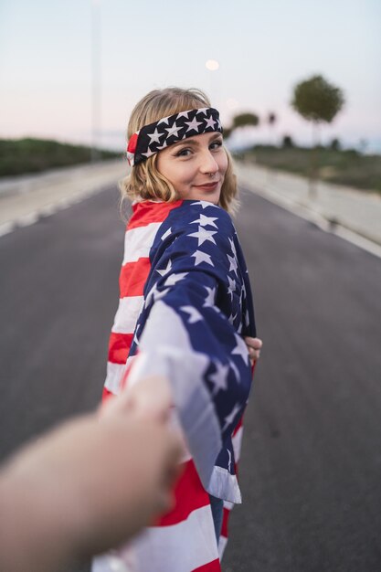 Joven mujer caucásica con la bandera de los Estados Unidos sobre sus hombros