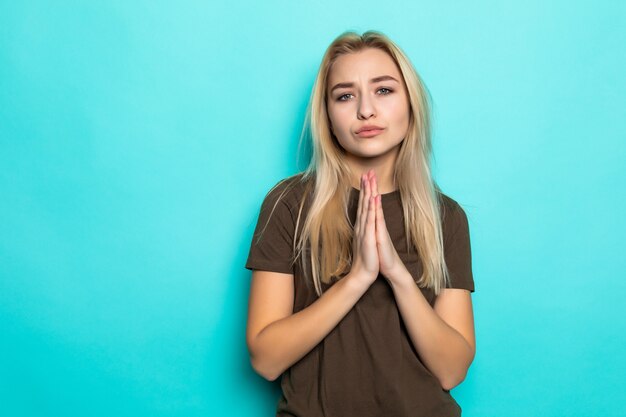 Joven mujer caucásica cogidos de la mano en rezar aislado en la pared azul